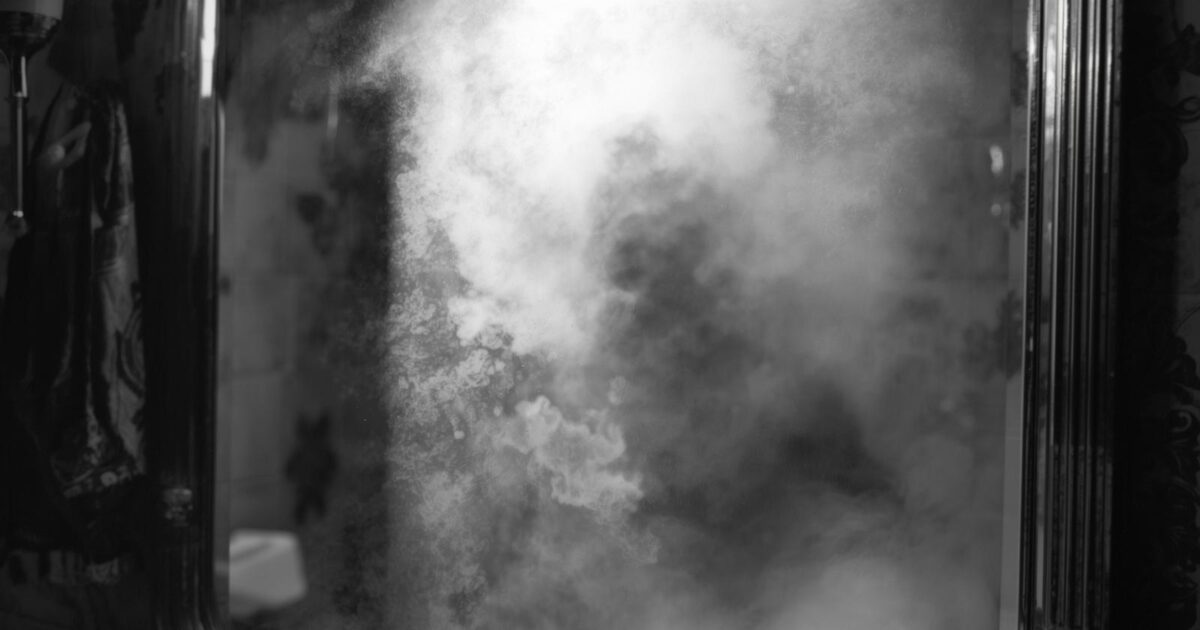 Image générée par IA. Comme une photographie réaliste en noir et blanc. Un miroir embué. On aperçoit un déporté au corps très maigre