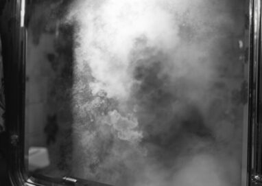 Image générée par IA. Comme une photographie réaliste en noir et blanc. Un miroir embué. On aperçoit un déporté au corps très maigre