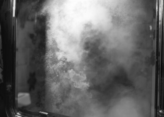 Image générée par IA. Comme une photographie réaliste en noir et blanc. Un miroir embué. On aperçoit un déporté au corps très maigre