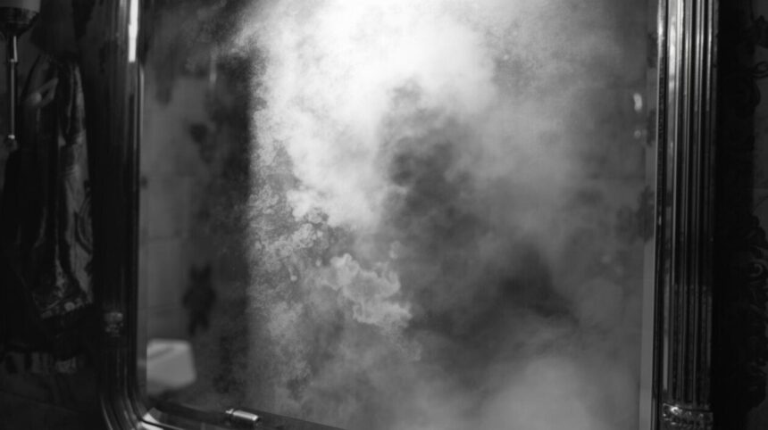 Image générée par IA. Comme une photographie réaliste en noir et blanc. Un miroir embué. On aperçoit un déporté au corps très maigre