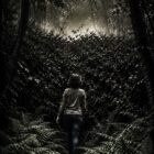 Une femme s'avance dans un bois et arrive devant une haute haie. Au-delà de la haie, une étrange lueur.