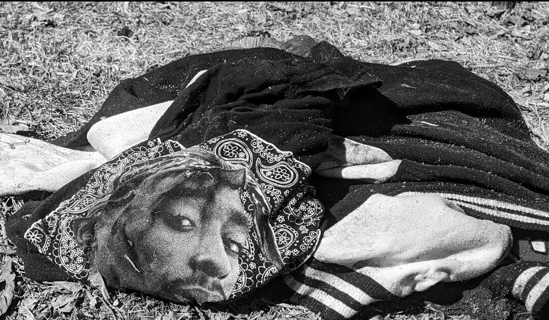 Photo de vêtements abandonnés sur un terrain vague. On voit un T-Shirt avec le visage d'un rappeur.